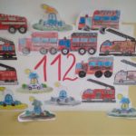Na ścianie wisi plakat z numerem alarmowym 112 oraz z pojazdami służb ratunkowych