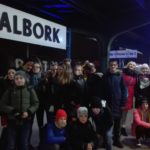 Uczestnicy wycieczki pod tablicą z napisem Malbork