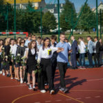Uczniowie klas ósmych tańczą poloneza na boisku szkolnym
