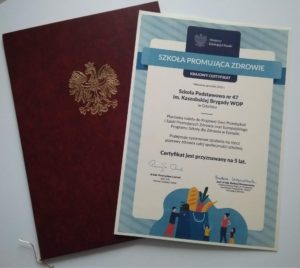 Na tle etui z Godłem Polski leży Krajowy Certyfikat Szkoły Promującej Zdrowie nadany SP 47 w Gdańsku. 