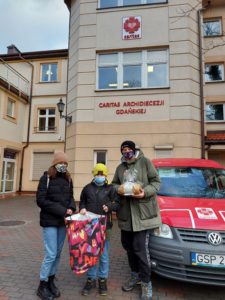 Wolontariusze stoją przed siedzibą Caritas w Sopocie i trzymają w ręku torbę pełną prezentów dla Chorych.