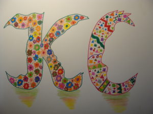 Praca przedstawia dwie litery "K" i "C". Litery ozdobione są kolorowymi kwiatkami i plamkami.