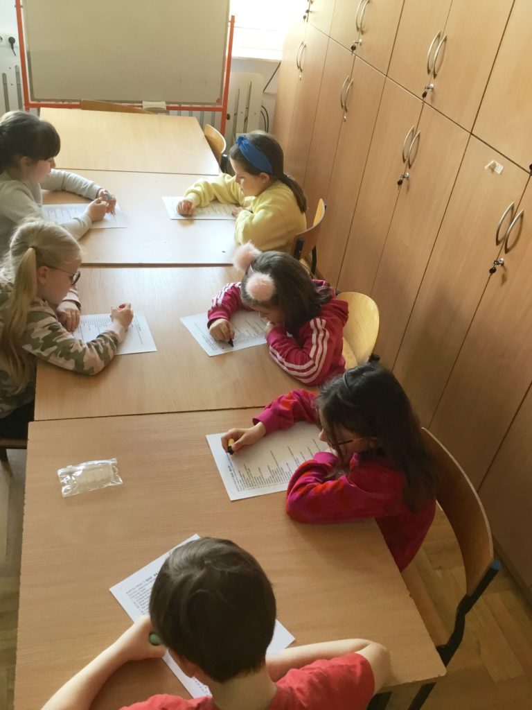 dzieci z klas młodszych w bibliotece wykonują pracę i rozwiązują zagadki z okazji Dnia Książki