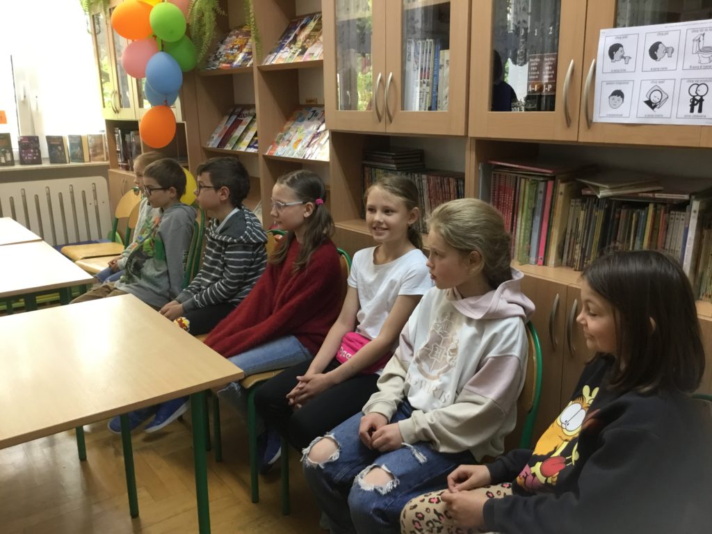 Uczestnicy zgromadzeni w bibliotece szkolnej słuchają zasad oceniania konkursu pięknego czytania