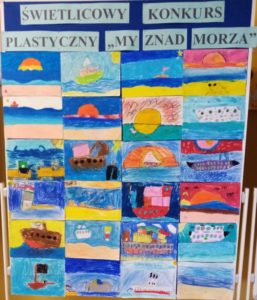 Na szkolnym korytarzu stoi niebieska tablica z napisem: "Świetlicowy Konkurs Plastyczny -My znad morza", na której są zawieszone prace plastyczne dzieci.