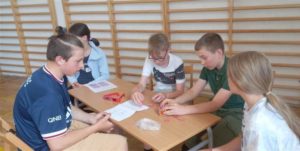 Uczniowie klasy 6B siedzą przy stoliku i rozwiązują zadanie matematyczne. Składają model graniastosłupa z plastikowych elementów.