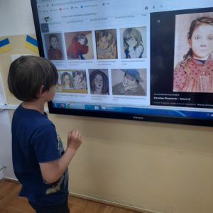 Uczeń stoi przed telewizorem, na którym wyświetlane są portrety polskich malarzy 