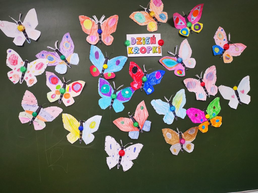 Na szkolnej tablicy, dookoła napisu Dzień Kropki umieszczono wykonane przez uczniów kolorowe papierowe motyle