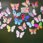 Na szkolnej tablicy, dookoła napisu Dzień Kropki umieszczono wykonane przez uczniów kolorowe papierowe motyle