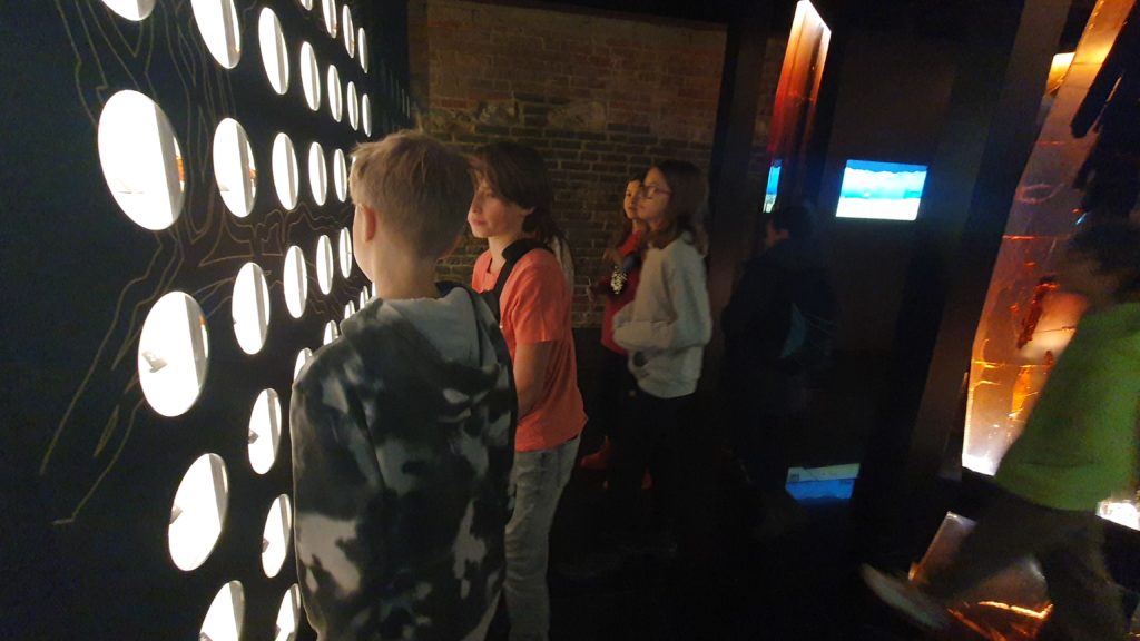 Czworo uczniów przygląda się eksponatom muzealnym umieszczonym w okrągłych okienkach.
