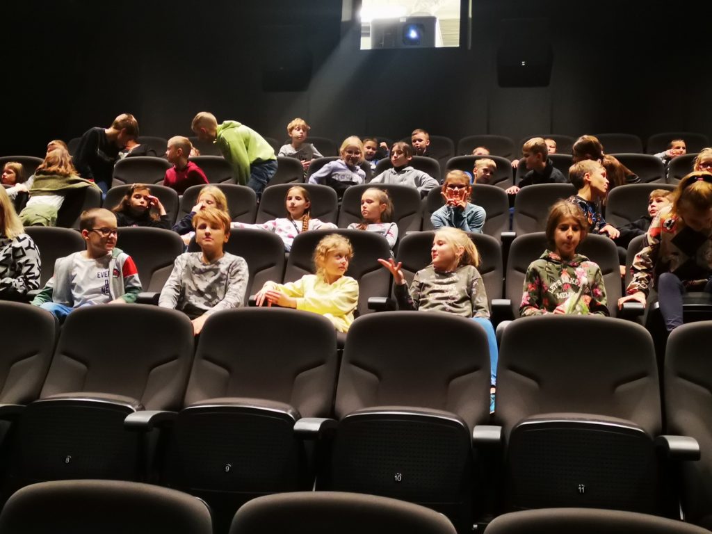 Uczniowie siedzą na fotelach w sali kinowej muzeum.