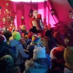 W udekorowanej sali stoi obrócona tyłem grupa uczniów klasy 1c. W tle elf i Mikołaj z akordeonem. 