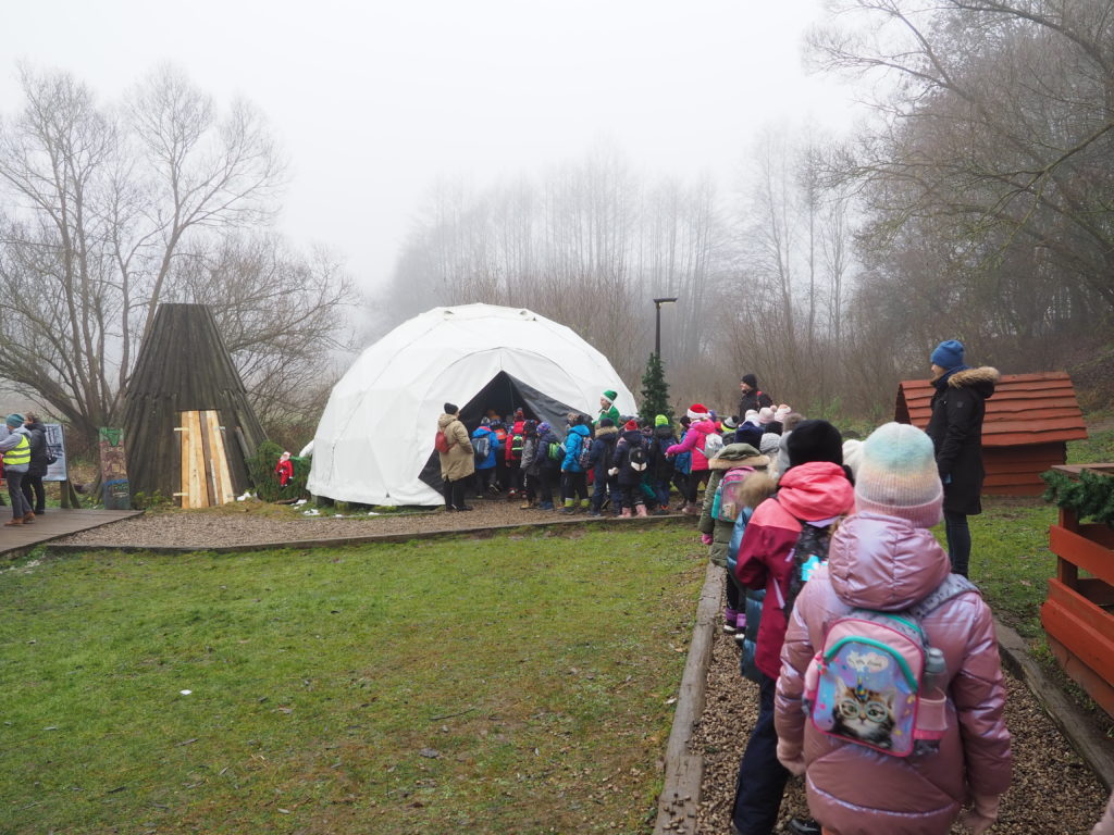 Uczniowie gęsiego ustawieni na ścieżce z kamieni przed wejściem do namiotu imitującego igloo. Pomiędzy nimi opiekunowie i nauczycielki oraz kobieta przebrana za elfa.