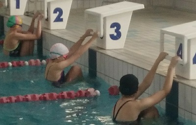 Trzy pływaczki ustawione do startu do stylu grzbietowego na trzech kolejnych torach 2, 3, 4