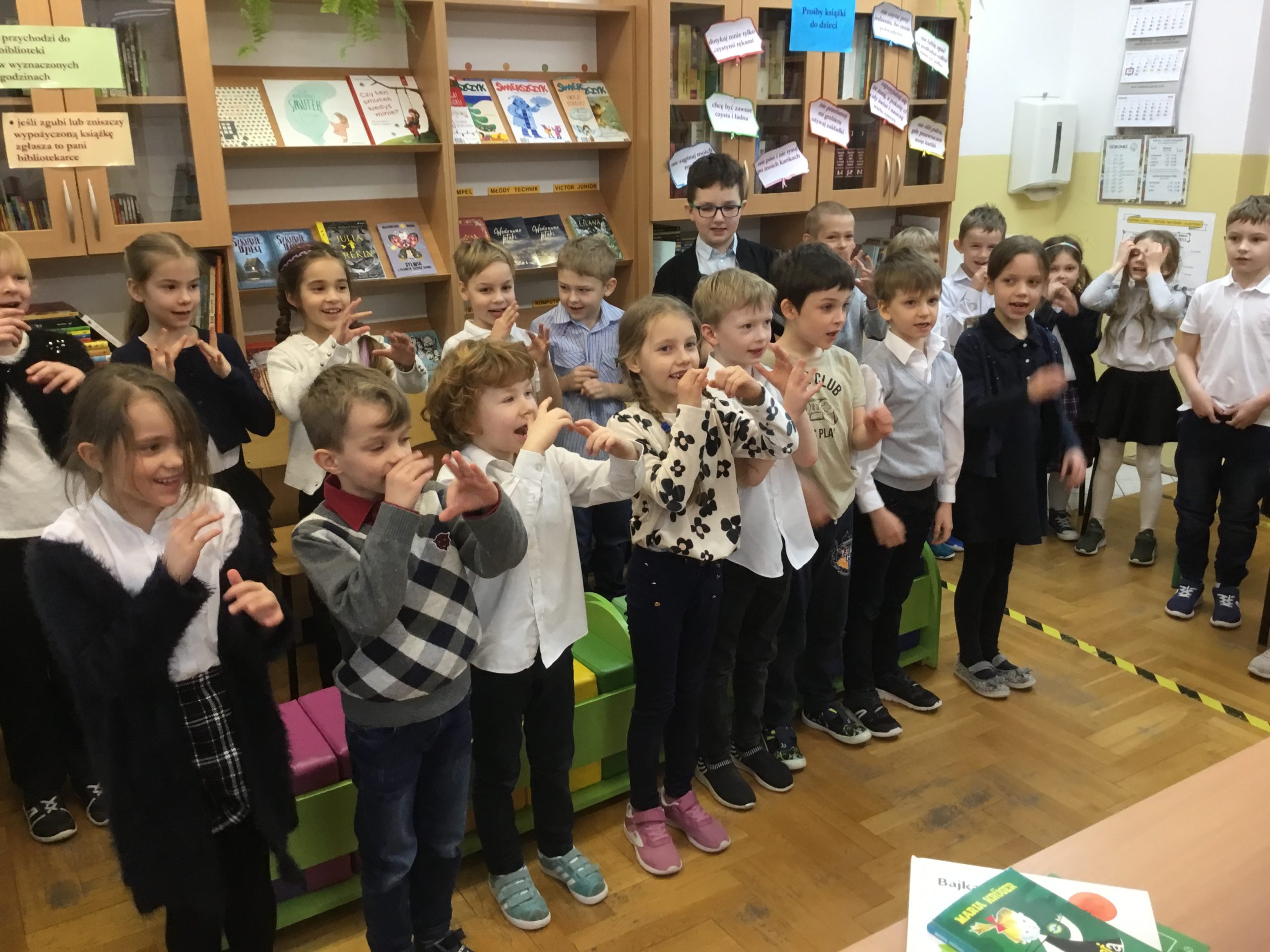 Klasa pierwsza B podaczas gestykulowania i  śpiewania  piosenki w bibliotece szkolnej