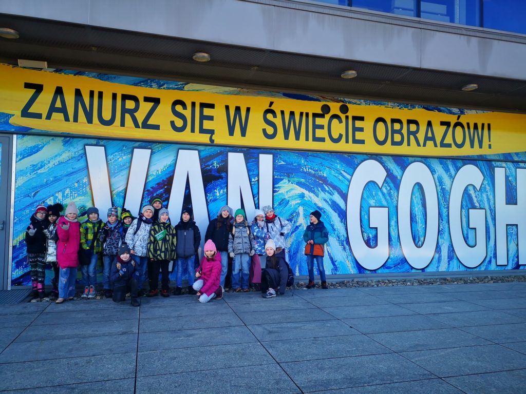 ucznowie z klasy 3a stoją przed budynkiem, w tle słoneczniki i napis Van Gogh zanurz się w świecie obrazów
