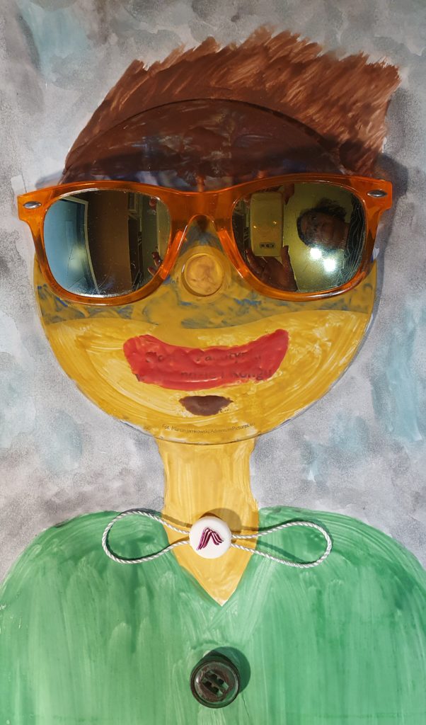 w centralnej części pracy namalowany portret chłopca, na twarzy którego przyklejone są słoneczne okulary