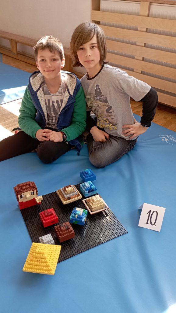W sali gimnastycznej na niebieskim materacu siedzi dwoje uczniów z klasy III. Przed nimi stoi ich budowla z klocków LEGO i etykietka z liczbą 10.