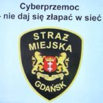 Na błękitnym tle jest logo Straży Miejskiej w Gdańsku. U góry zdjęcia jest czarny napis „Cyberprzemoc-nie daj się złapać w sieć”