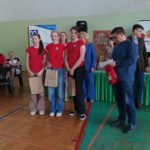 3 uczennice SP 47 w czerwonych koszulkach z nagrodą w rękach stoją na tle plakatu XV Ogólnopolskiego Konkursu „Ratujemy życie”, obok organizatorzy konkursu. W tle siedzą na krzesłach ratownicy- członkowie jury konkursowego.