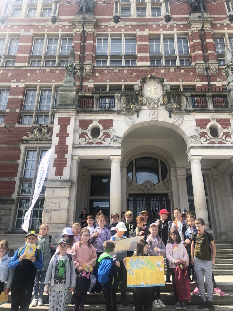 24 uczniów stoi na schodach przed budynkiem architektury Politechniki Gdańskiej.