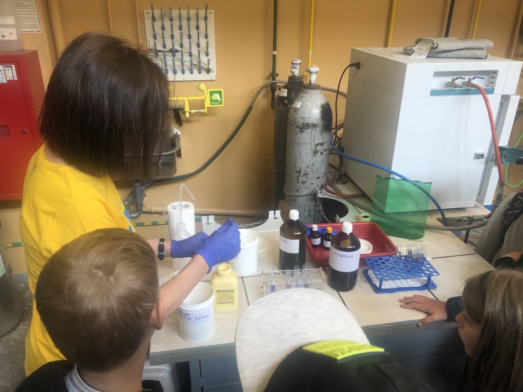 Trójka dzieci przygląda się doświadczeniu chemicznemu przeprowadzanemu przez pracownika Katedry Chemii PG.
