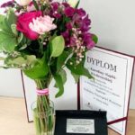 na stole stoi wazon z kwiatami, dyplom oraz pudełko z piórem wiecznym.