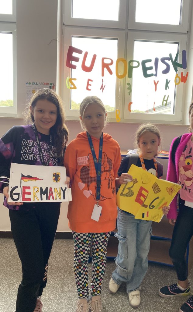 Grupa uczniów stoi na korytarzu z przewodnikami państw przygotowanych przez dzieci. A tle widnieje napis Europejski Dzień Języków Obcych