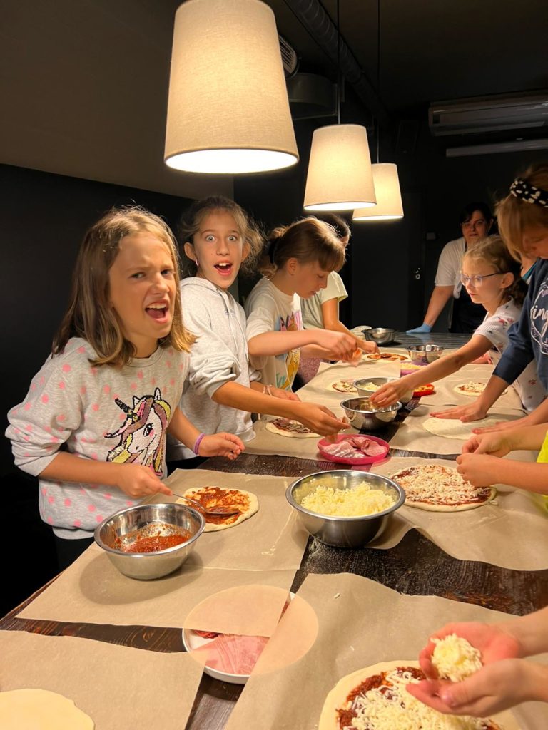 grupa dziewczyn stoi przy stole i robi pizzę