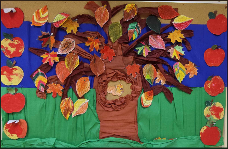 Tablica ścienna przedstawia jesienne drzewo z bibuły z pracami plastycznymi dzieci- liście i jabłka pokolorowane lub wyklejone plasteliną. 