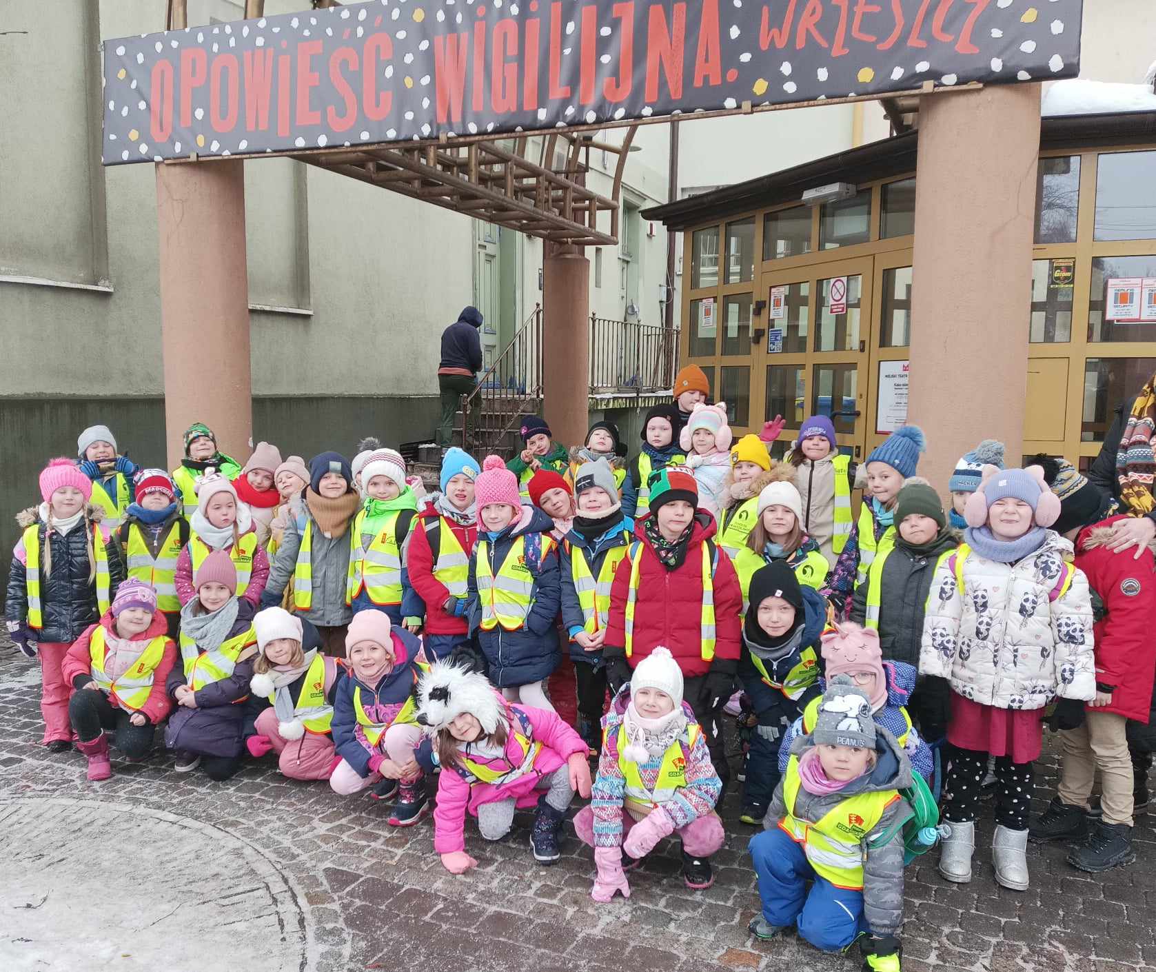 Grupa około 40 dzieci z uśmiechem na twarzy stoi przed wejściem do Teatru Miniatura.