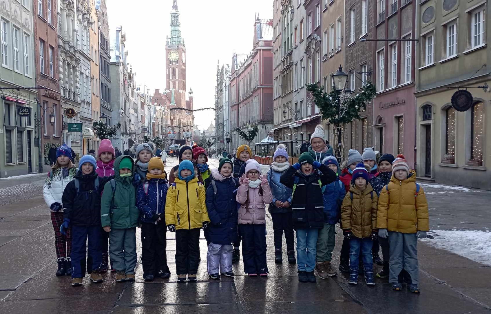 Na ulicy Długiej w Gdańsku stoi 20 uczniów klasy 2c wraz z wychowawcą w dwóch rzędach. W tle kamienice i Ratusz Miasta.