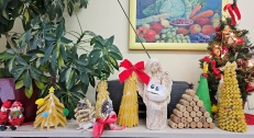 Na półce stoją wykonane już choinki z różnych materiałów. Od lewej cztery z makaronów i ozdób świątecznych, w środku figurka aniołka a po prawej z korków i znowu z makaronów.