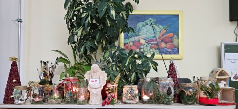 Lampiony ze słoika stoją ustawione na półce w pierwszym rzędzie. Za nimi od lewej z tyły czerwona doniczka z kwiatem, na środku figurka aniołka a po prawej domek ceramiczny.
