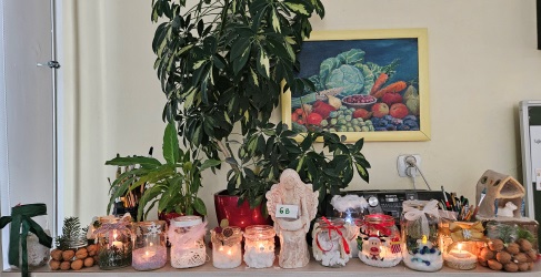 Lampiony ze słoika stoją ustawione na półce w pierwszym rzędzie. Za nimi od lewej z tyły czerwona doniczka z kwiatem, na środku figurka aniołka a po prawej domek ceramiczny.