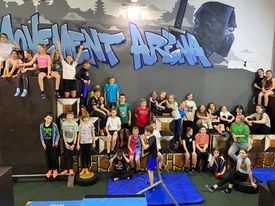 grupa uczniów w strojach sportowych siedzi lub stoi na tle ścianki z napisem Movement Arena