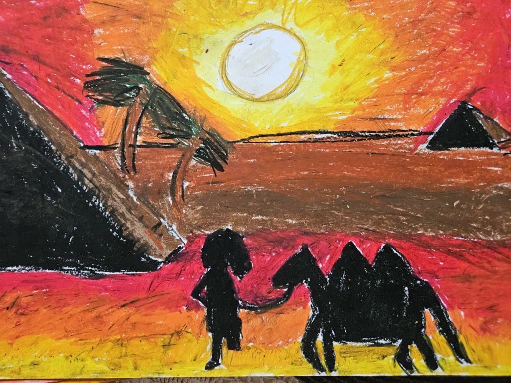Na pierwszym planie czarne sylwetki to człowiek prowadzący wielbłąda. Na drugim planie, po lewej stronie piramida z palmami. Na horyzoncie, po prawej stronie zarys piramidy. Na horyzoncie zachodzące słońce. Całość w gamie barw żółtych i pomarańczowych