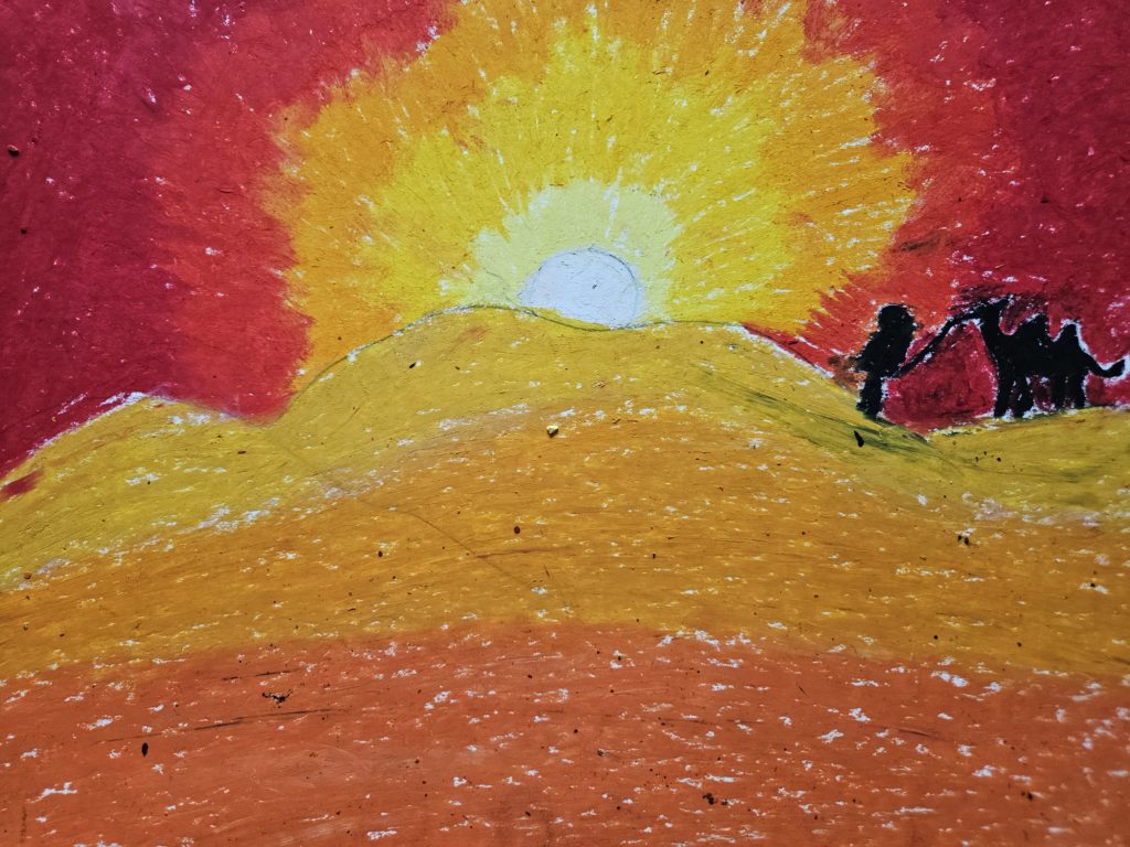 Na pierwszym planie żółte piaski pustyni. Na horyzoncie, po prawej stronie sylwetki czlowieka z wielbłądem. Na horyzoncie zachodzące słońce. Całość w gamie barw żółtych i różowych