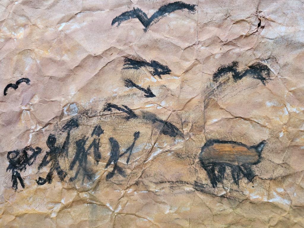 Praca inspirowana malarstwem paleolitu ze sceną z polowania. Na pierwszym planie, po lewej stronie zarysy ludzi, a po prawej uciekajacego zwierzęcia. Na niebie czarne, w locie ptaki