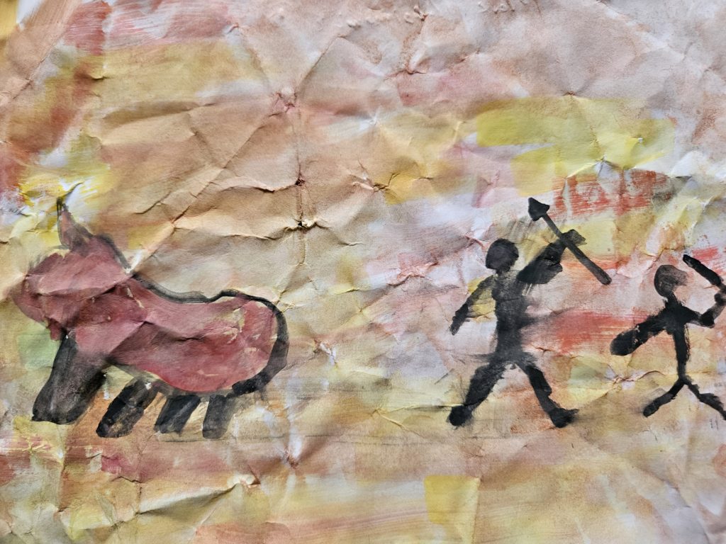 Praca inspirowana malarstwem paleolitu ze sceną z polowania. Na pierwszym planie, po prawej stronie zarysy biegnących ludzi, a po prawej uciekającego zwierzęcia