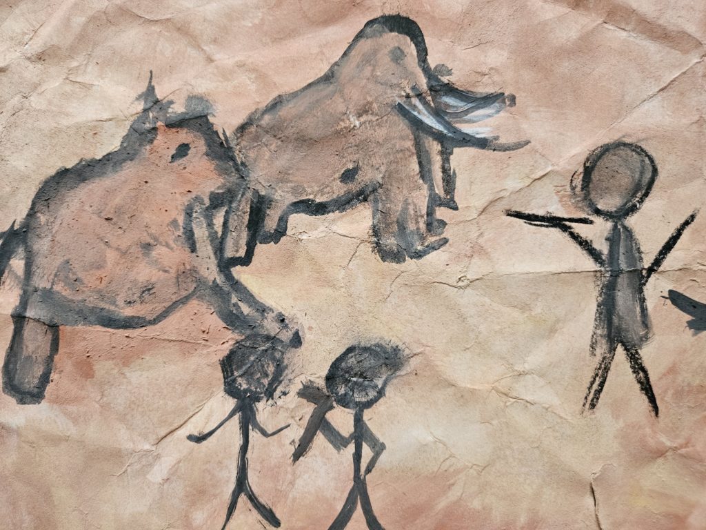Praca inspirowana malarstwem paleolitu ze sceną z polowania. Na pierwszym planie zarysy ludzi, a po lewej stronie galopujących mamutów