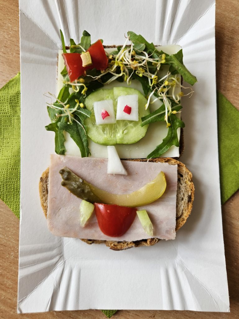 Na talerzyku „uśmiechniętą” kanapka z oliwkami, pomidorem, rukolą