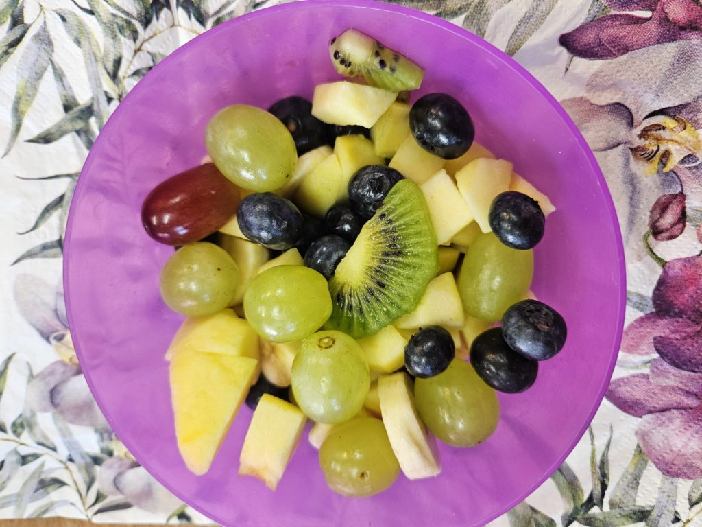 W miseczkach na serwetkach kolorowe, pokrojone różne owoce jak: banany, mandarynki, winogrona, truskawki