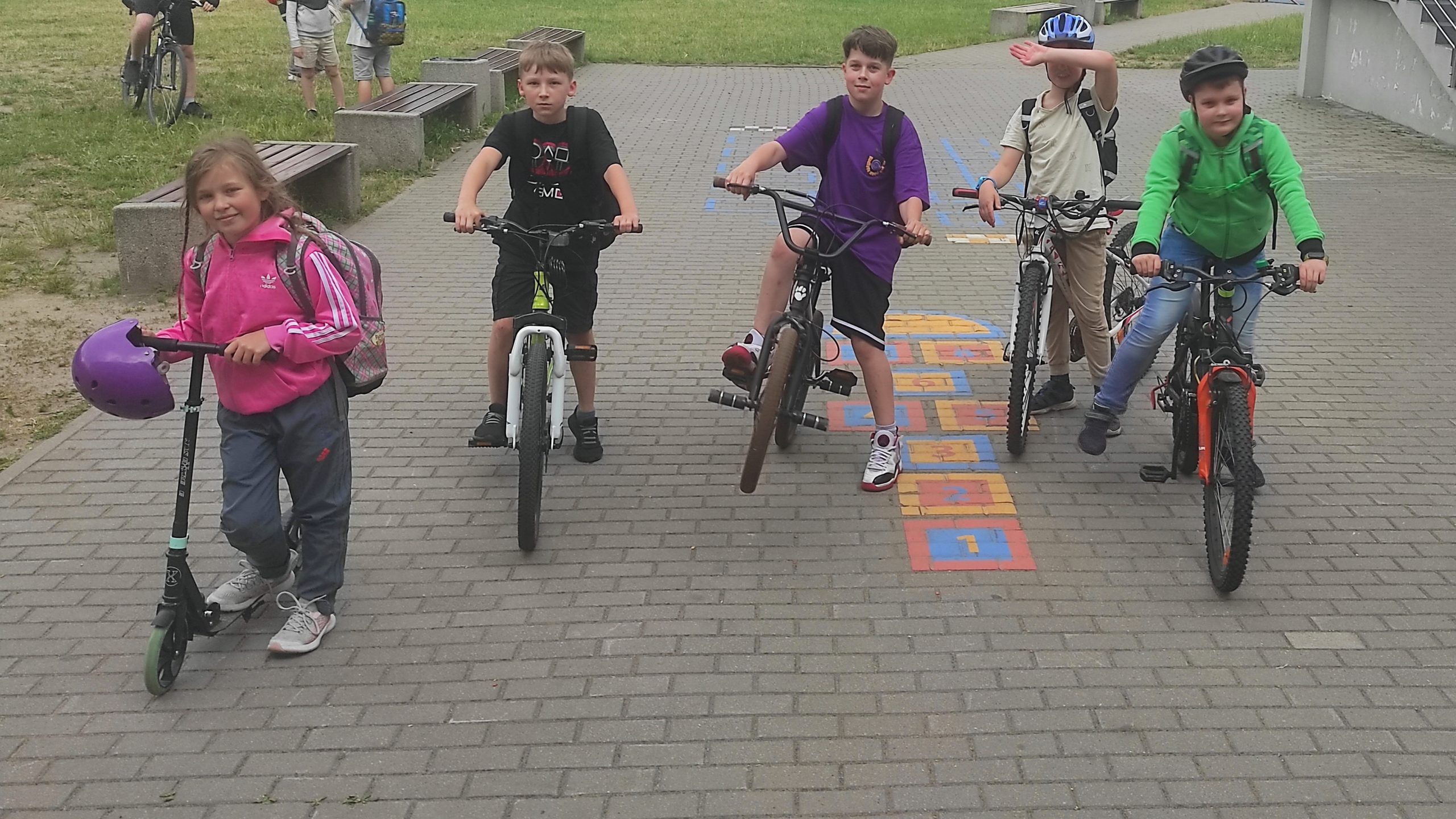 5 uczniów klasy 3b ustawionych w rzędzie. Od lewej dziewczynka na hulajnodze, pozostali chłopcy na rowerach.