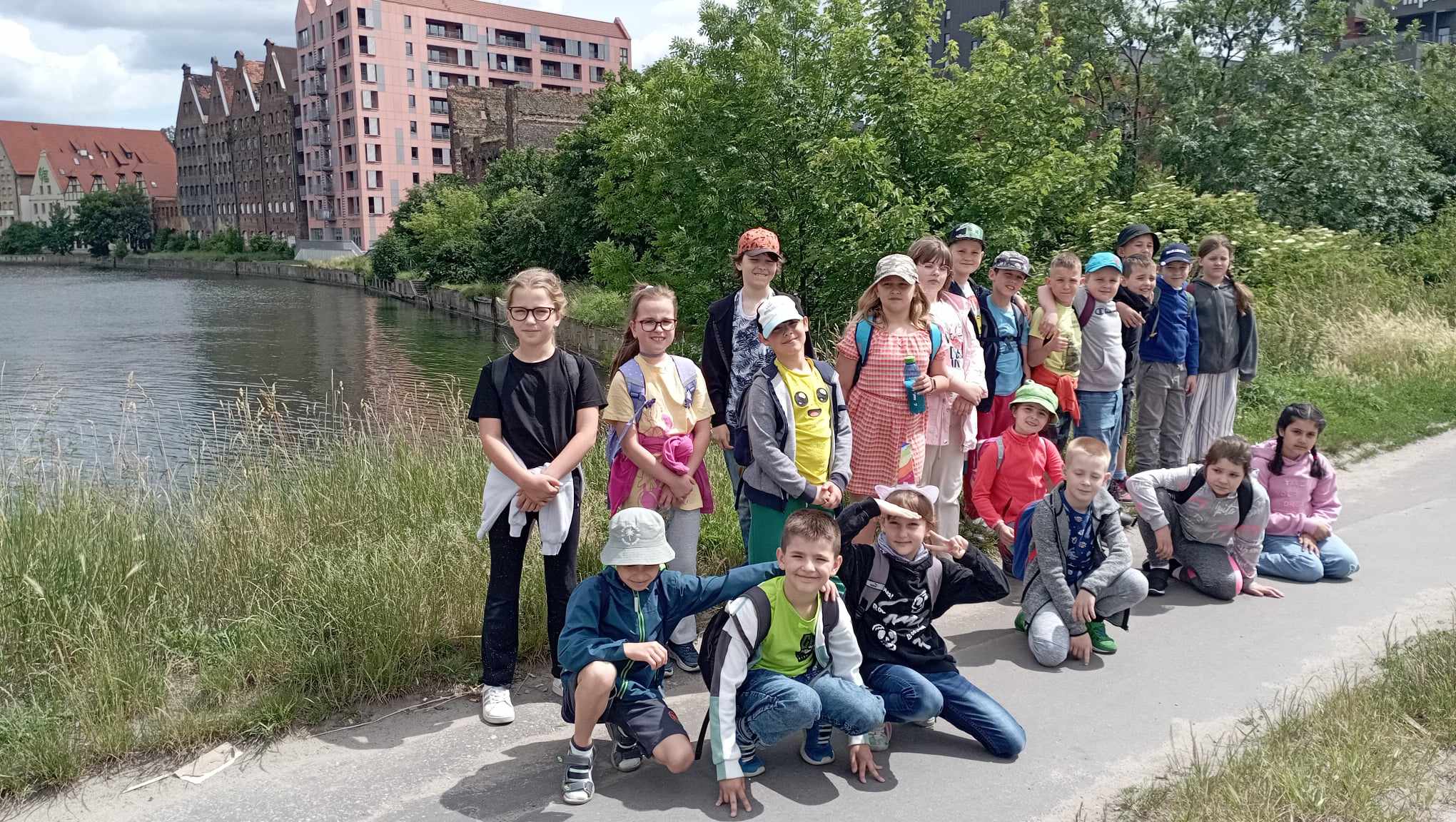 Na tle zieleni, rzeki i zabytkowych budynków stoją lub kucają ustawieni w dwa rzędy uczniowie klasy 2c.