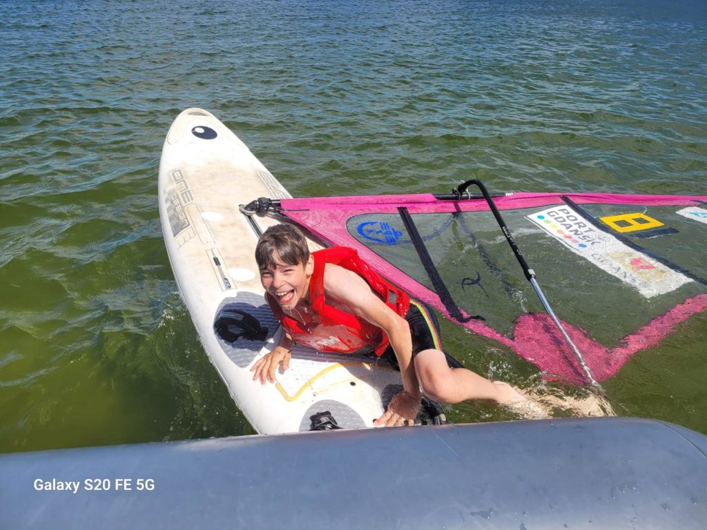 Chłopiec leży na desce windsurfingowej w wodzie