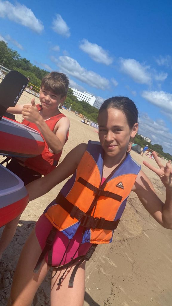 dwóch uczniów stoi na plaży koło desek do windsurfing