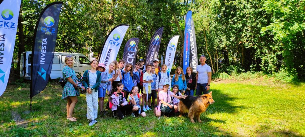 Grupa uczniów wraz na nauczycielem i trenerem stoi na trawie na tle banerów