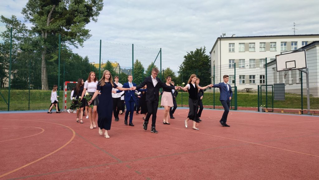 Uczniowie tańczący poloneza na boisku szkolnym.