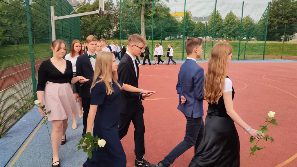 Uczniowie tańczący poloneza na boisku szkolnym.